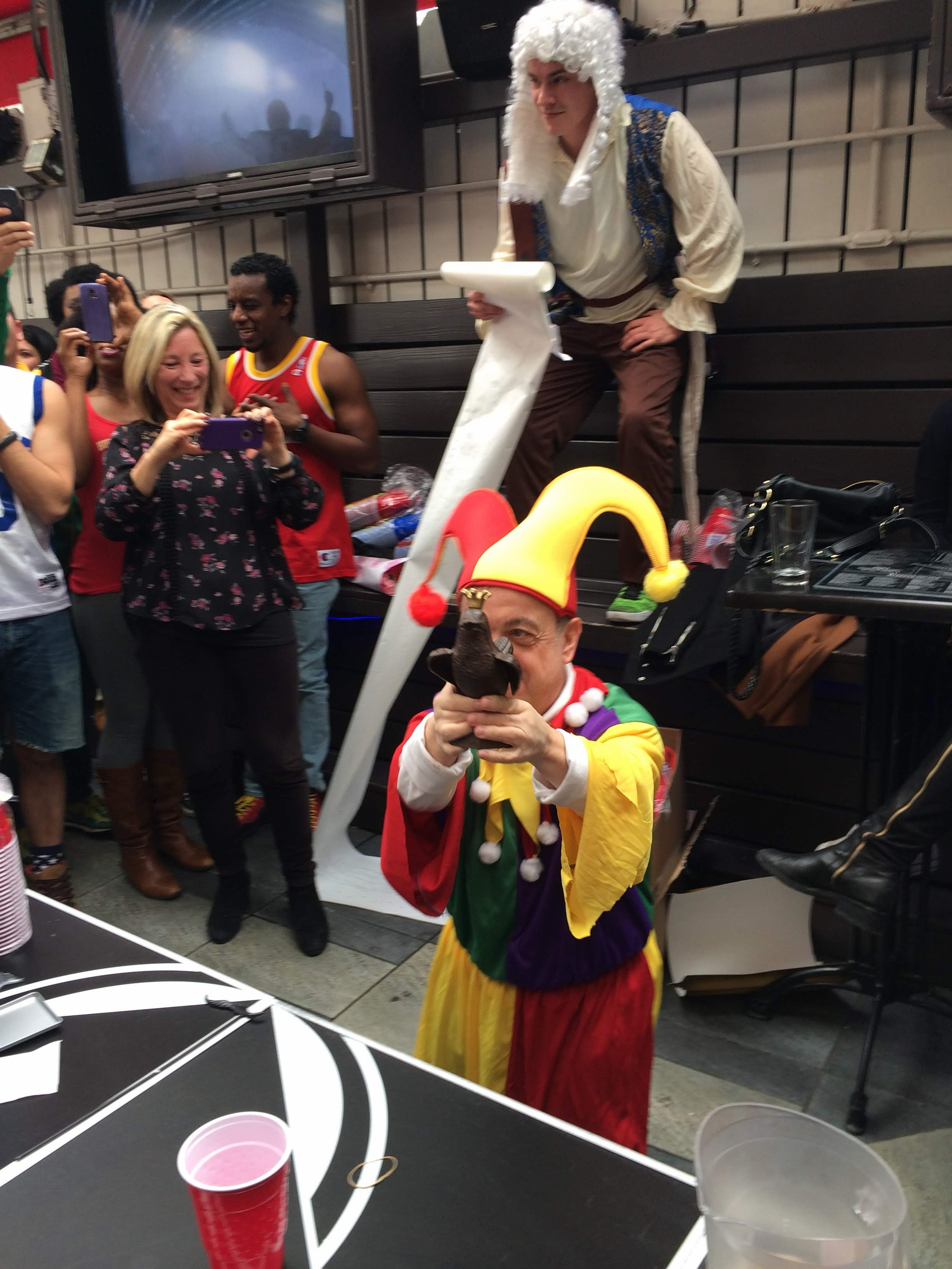 A 7H costume party — a man in a jester outfit drinking from a boot, another on stilts in colonial dress holding a giant number one