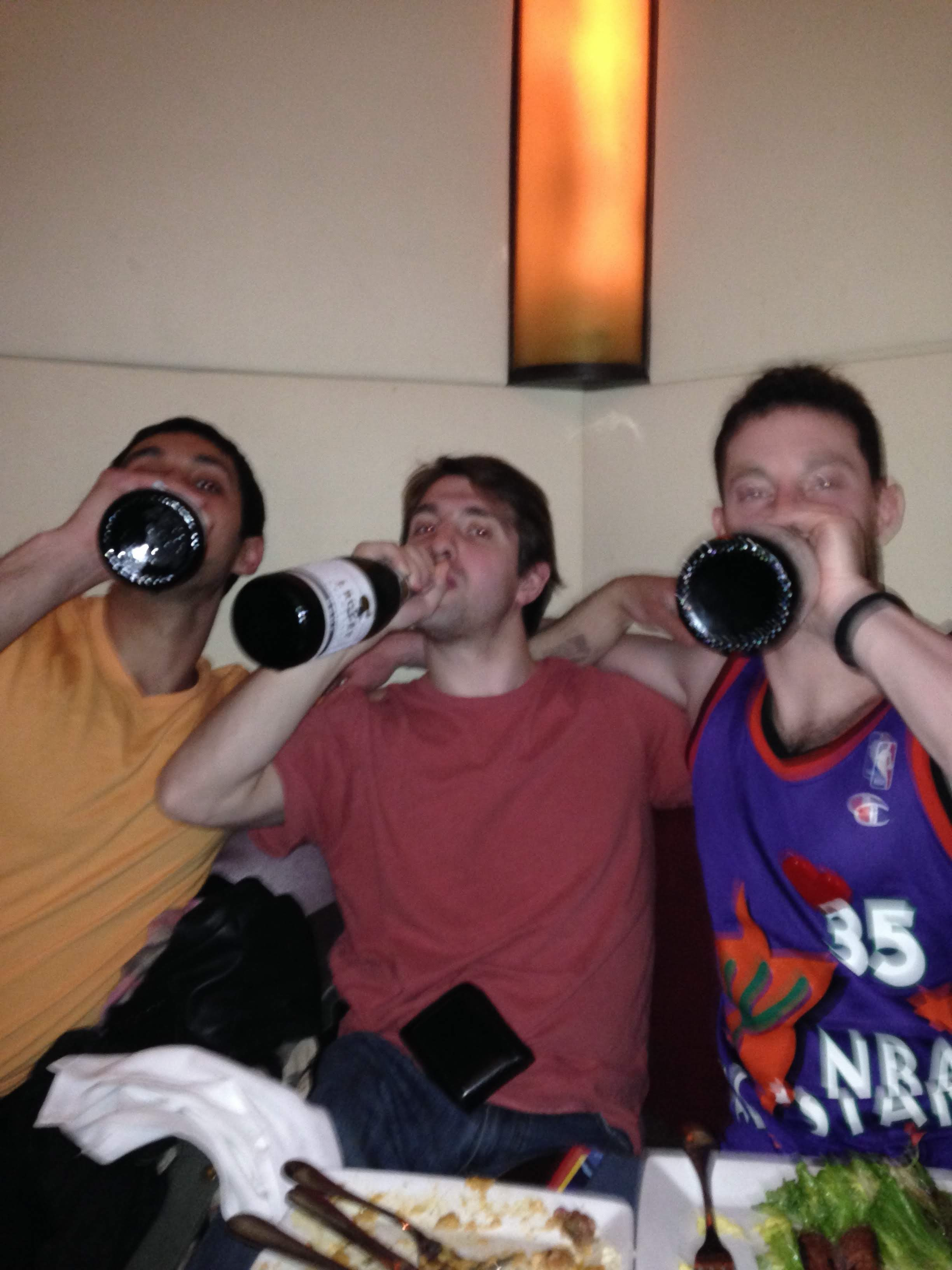 Three friends in a booth each chugging a bottle — Vivek in yellow, Matt Greyson in the center, ZA in a purple NBA jersey