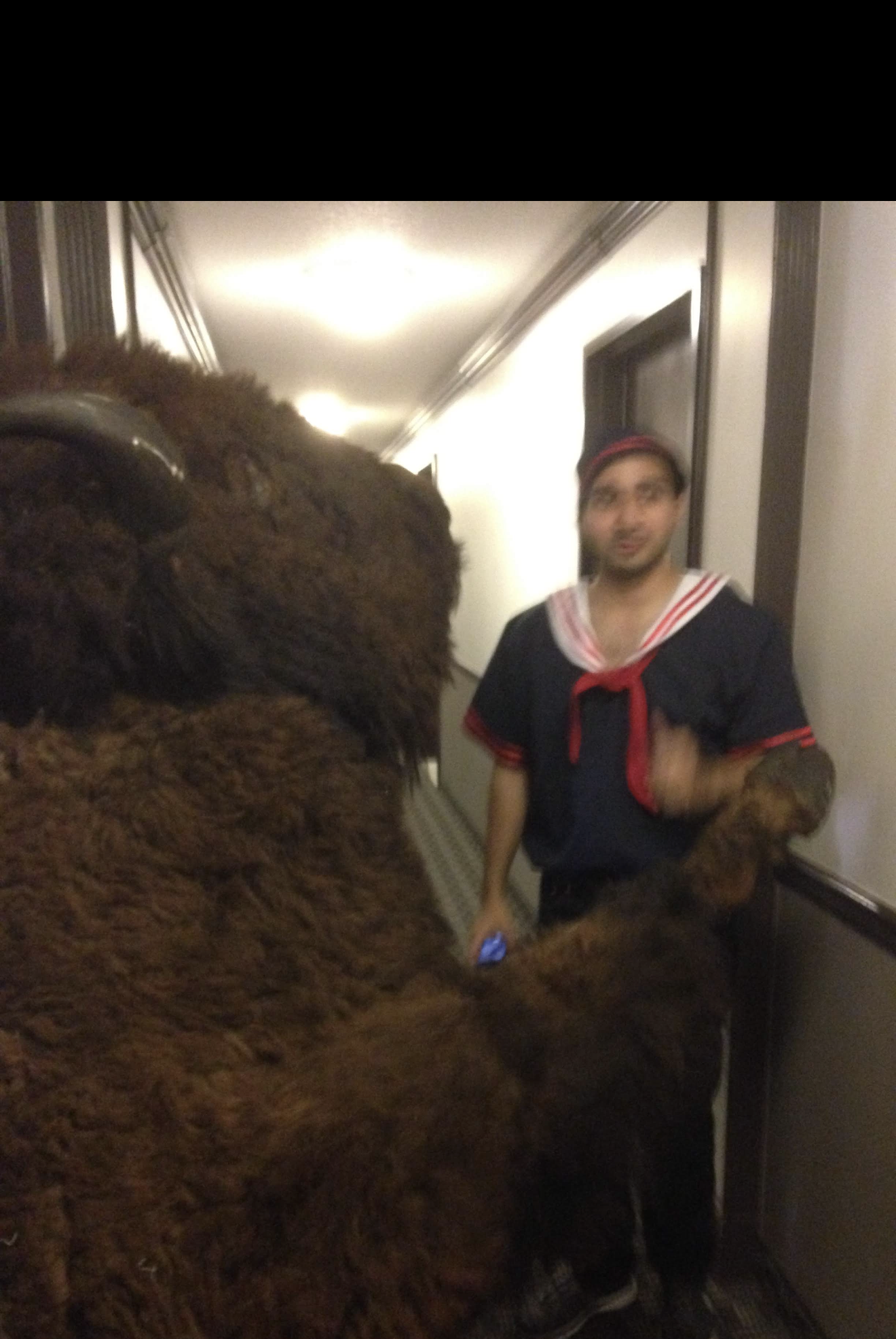 Waqas in a sailor costume standing next to the giant buffalo costume in an apartment hallway