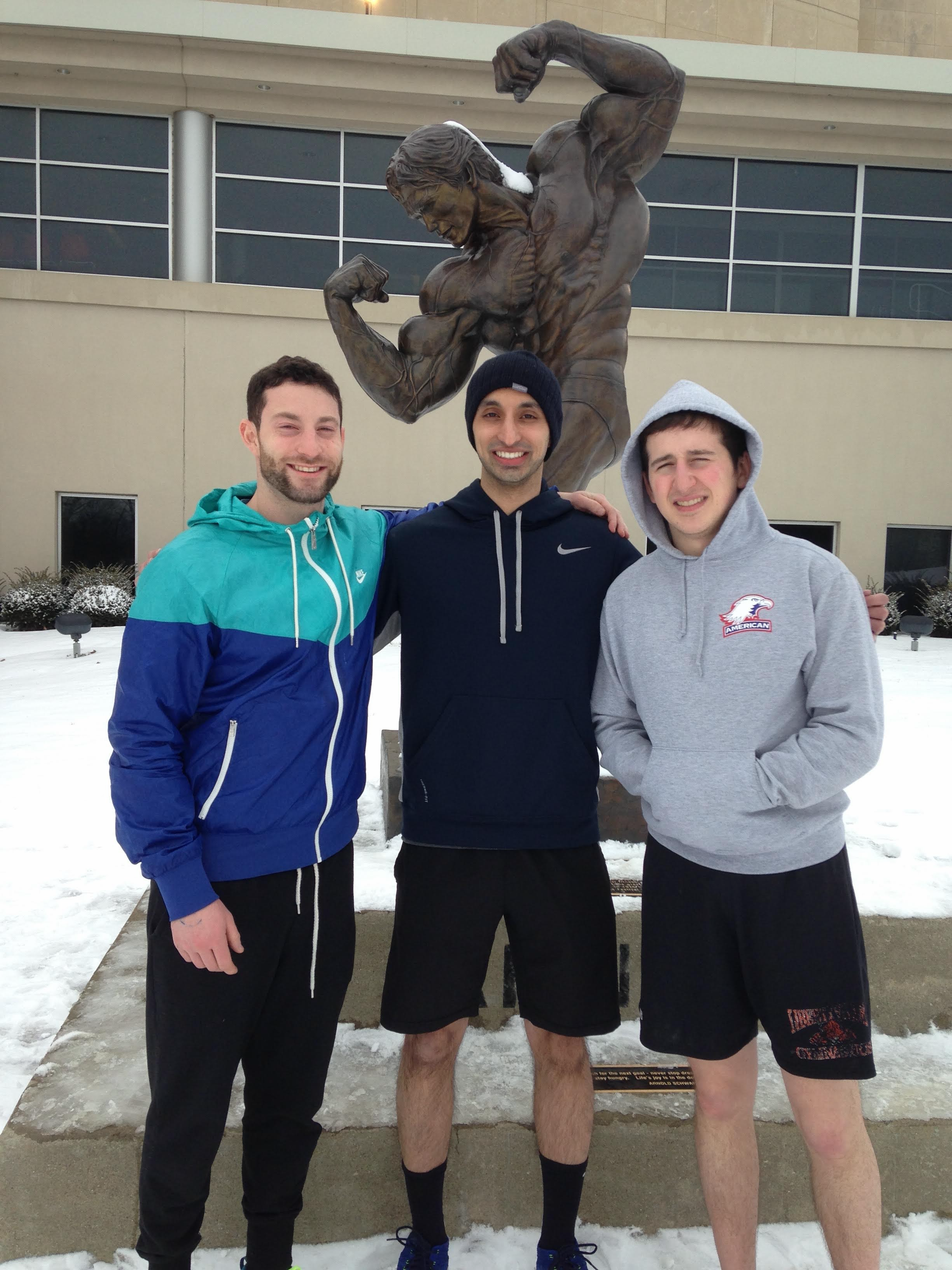 Three friends posing in front of the bronze Arnold Schwarzenegger bodybuilding statue in the snow