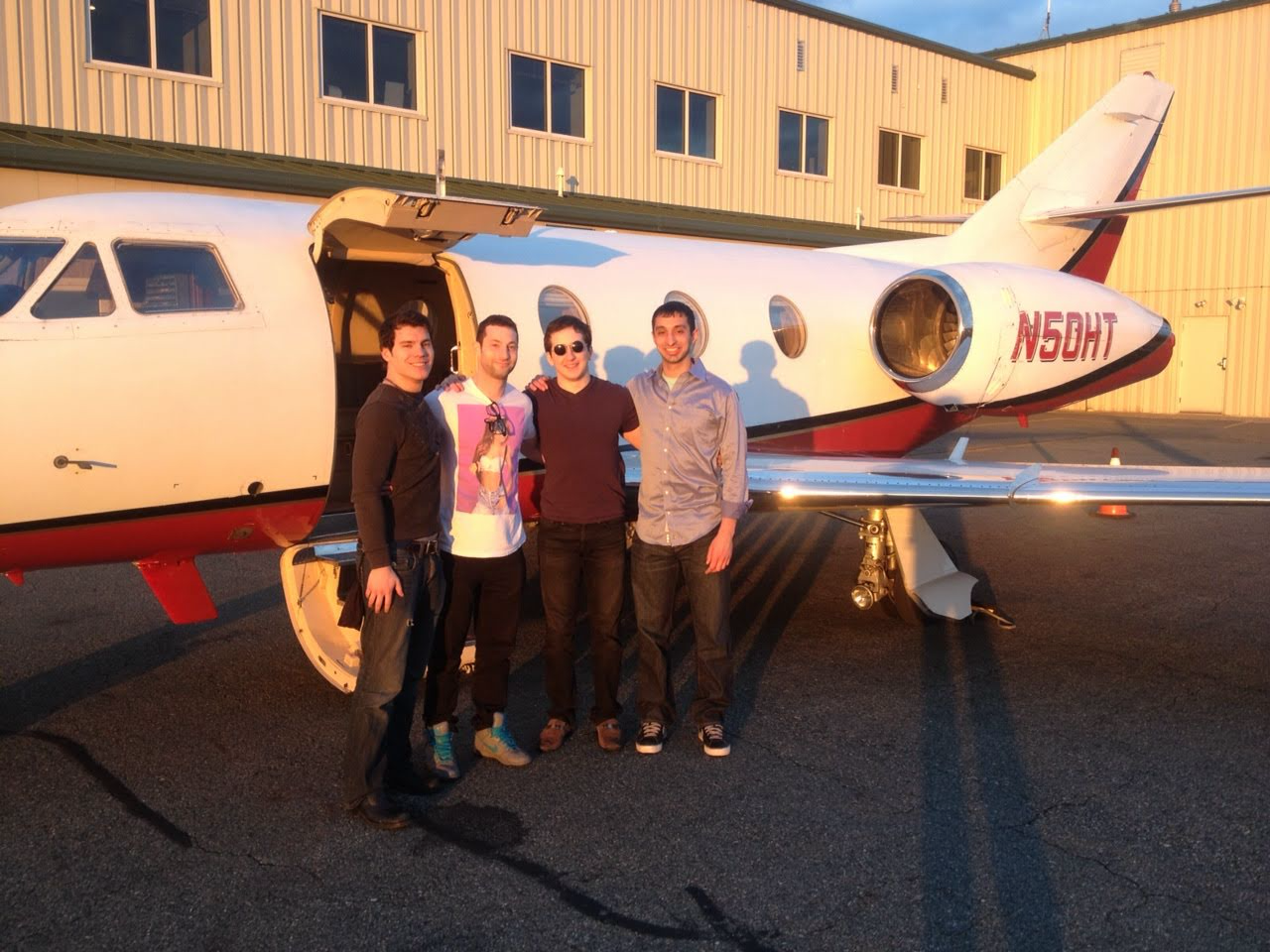 Vivek and three friends posing in front of a private jet (tail number N50HT) on a tarmac at sunset