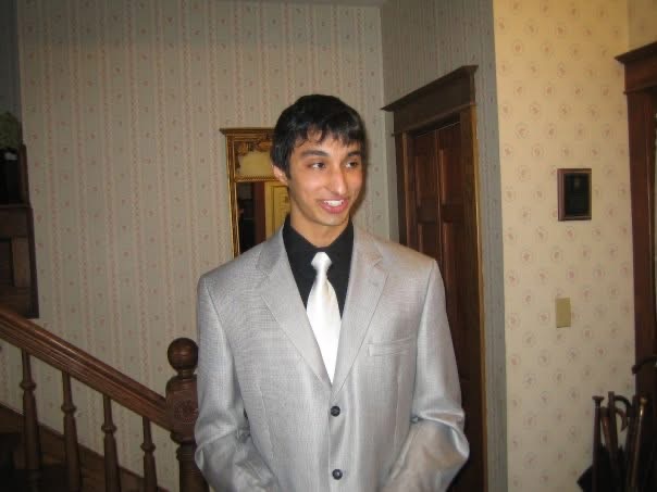 Vivek in a grey suit standing by a staircase before a dance