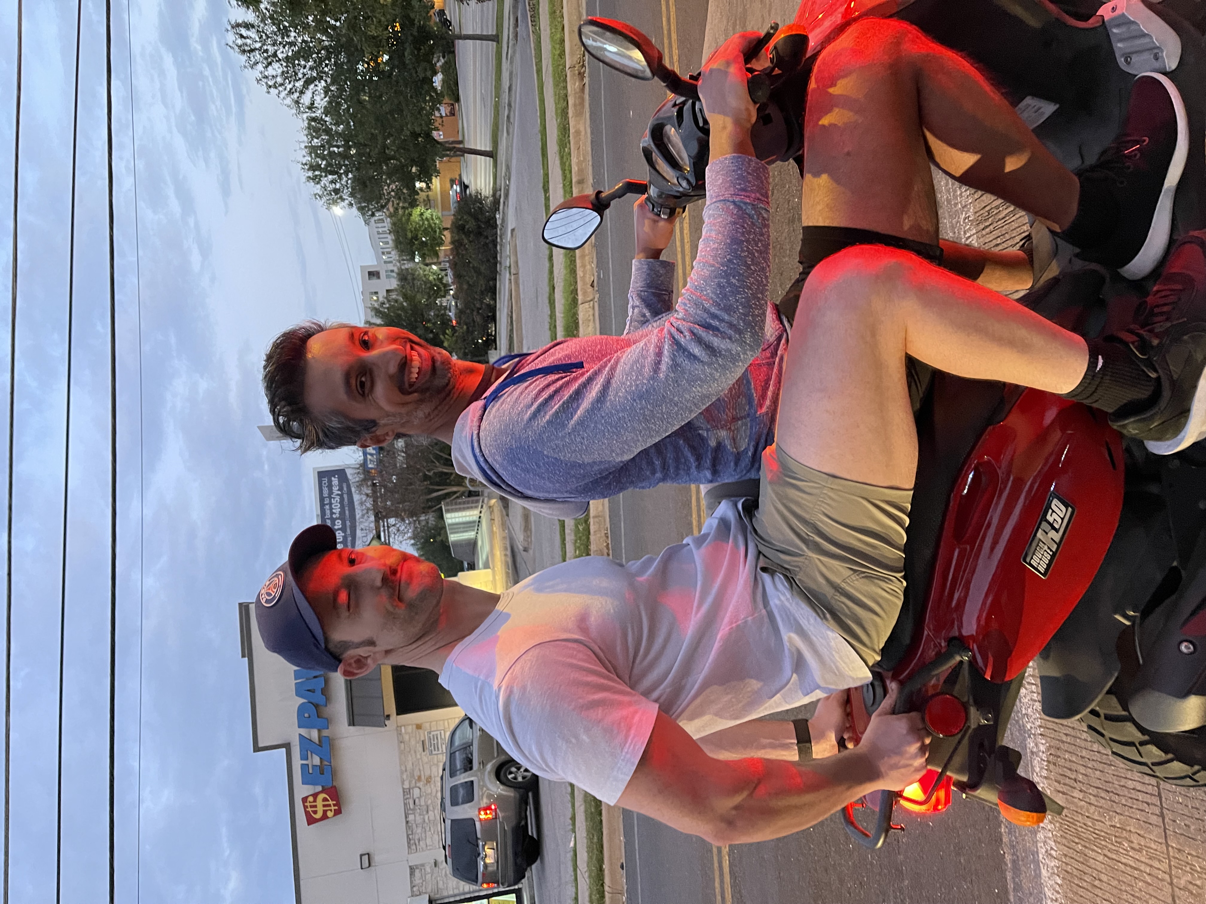 Vivek and Zack Aronson two-up on a red scooter in Austin at dusk