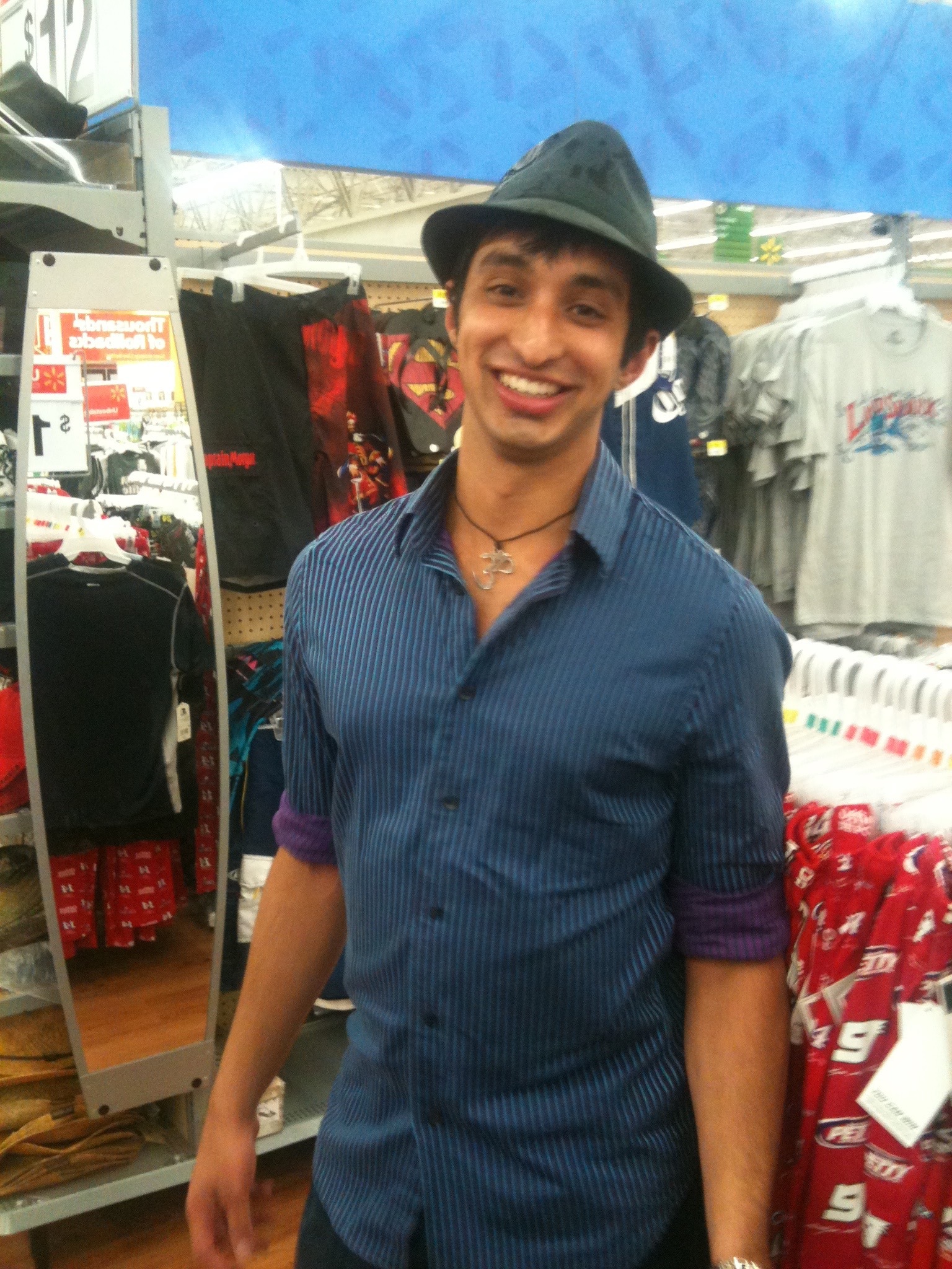 A young Vivek in a grey fedora and blue striped shirt, grinning inside a store