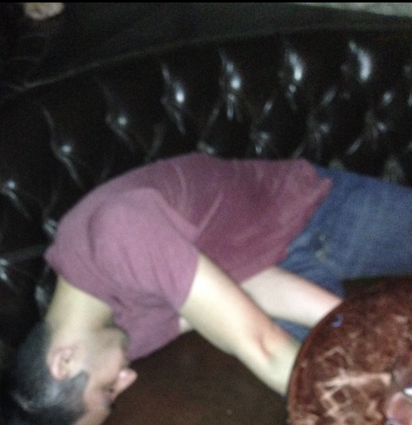 Vivek passed out face-down on a black tufted-leather club booth at night