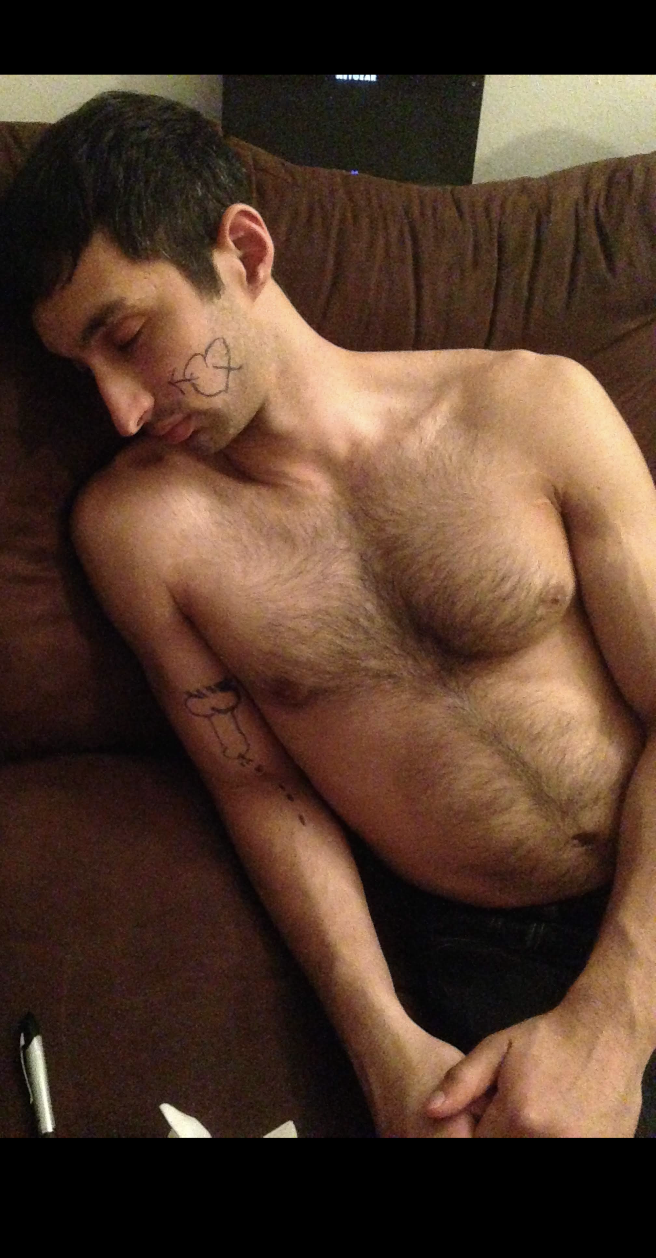 Vivek asleep shirtless on a couch with marker doodles on his face and arm, a Sharpie nearby